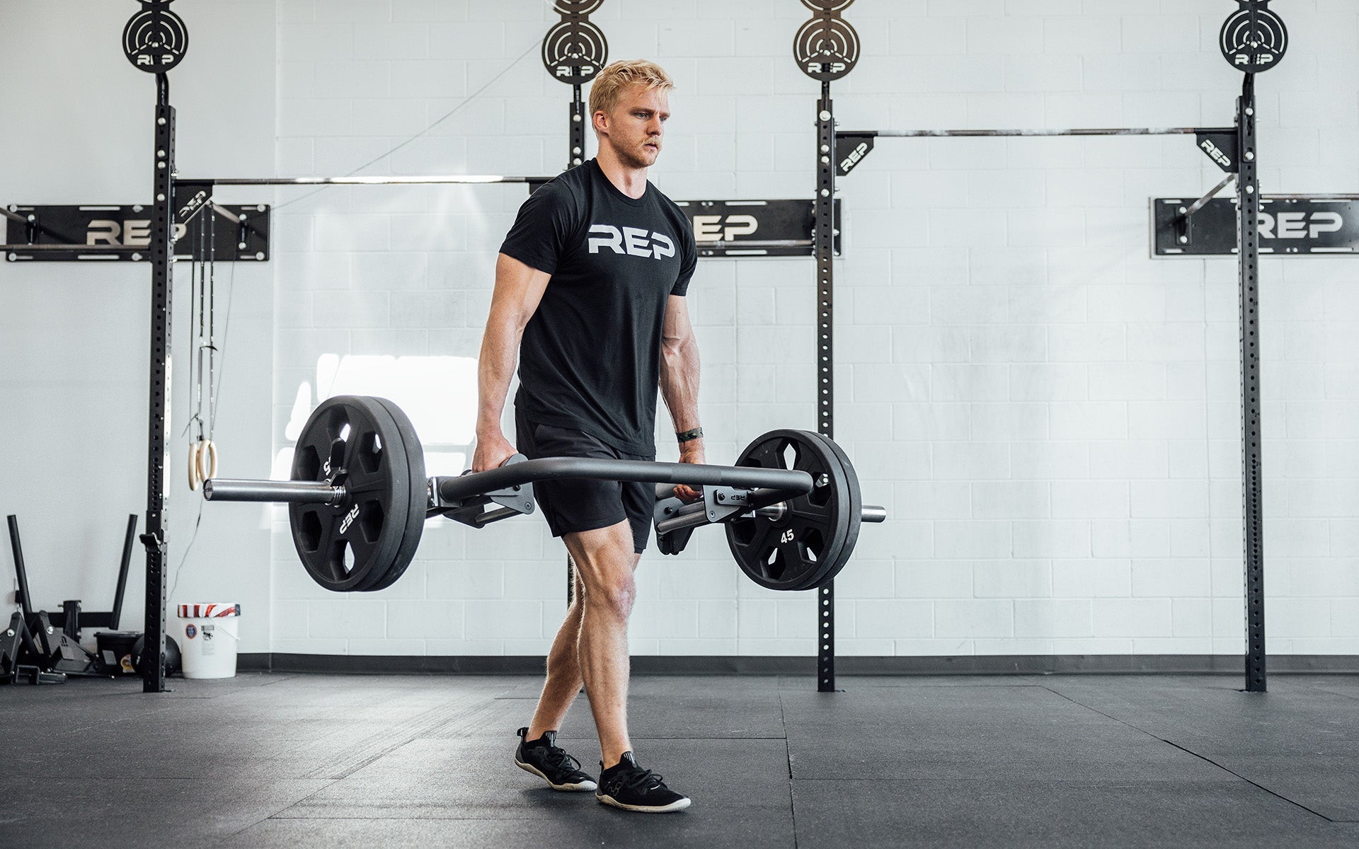 Male athlete performing a farmers carry with the REP Open Trap Bar.